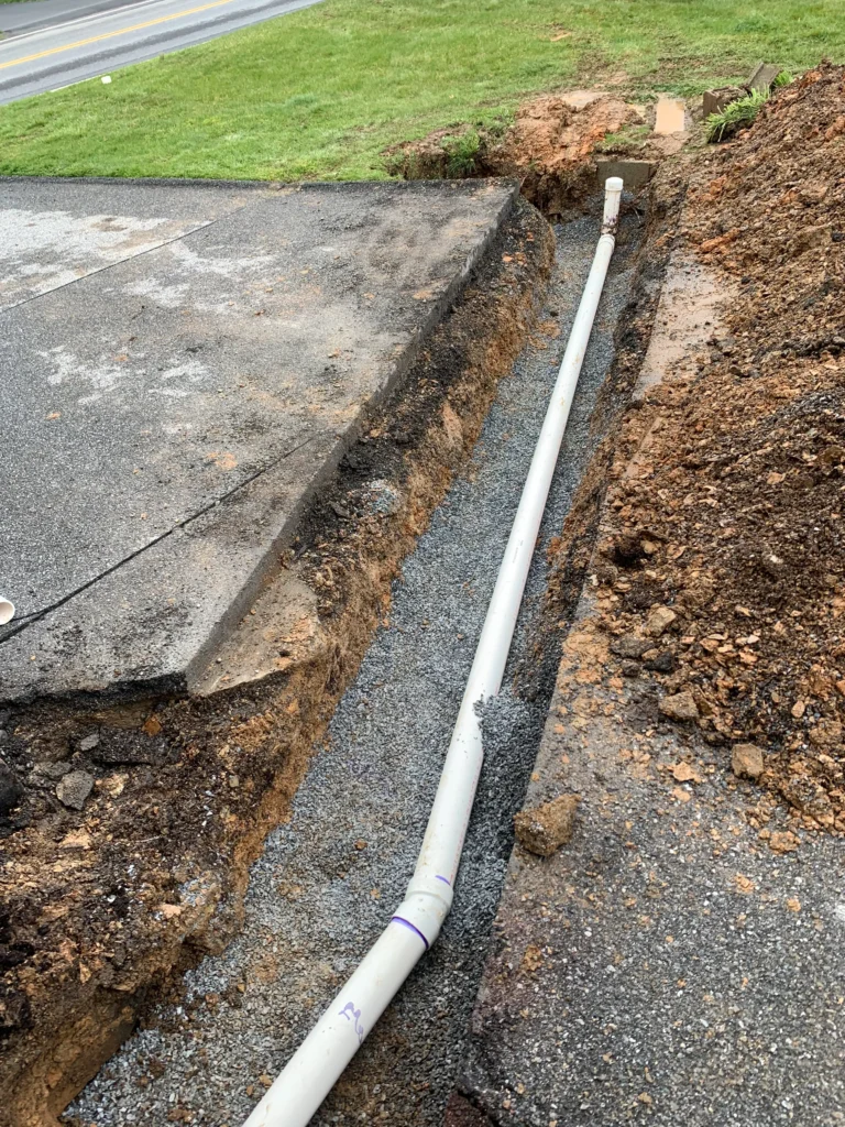 A worker installs a pipe in the ground adjacent to a road, showcasing construction activity in the area.