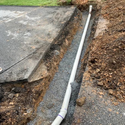 A worker installs a pipe in the ground adjacent to a road, showcasing construction activity in the area.